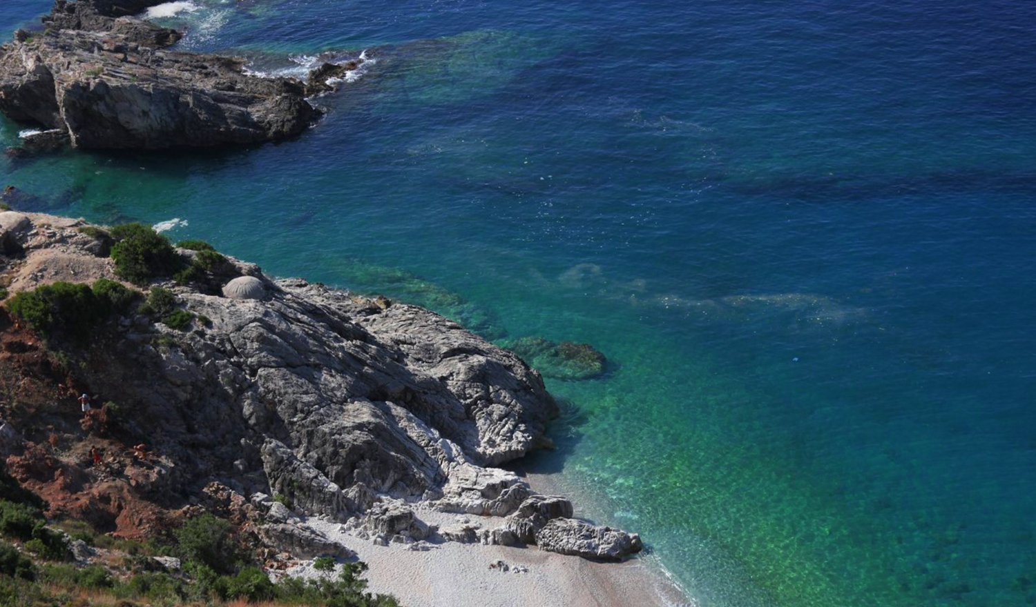 Aquarium Bay Albania — volcanic rock cliffs framing crystal-clear turquoise Ionian water