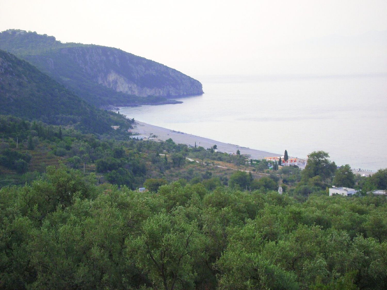 Dhërmi Beach Albania — long white pebble crescent with deep blue Ionian water and mountain backdrop