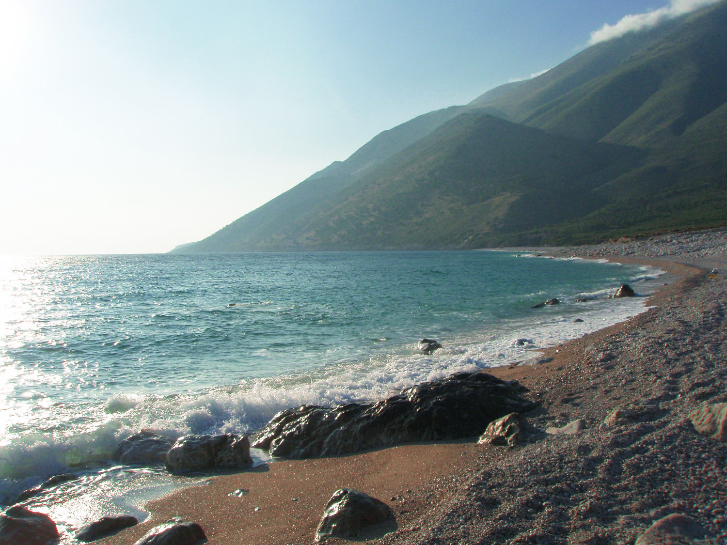 Dhërmi Beach Albania — swimmers in crystal-clear turquoise water with rocky mountain cliffs above