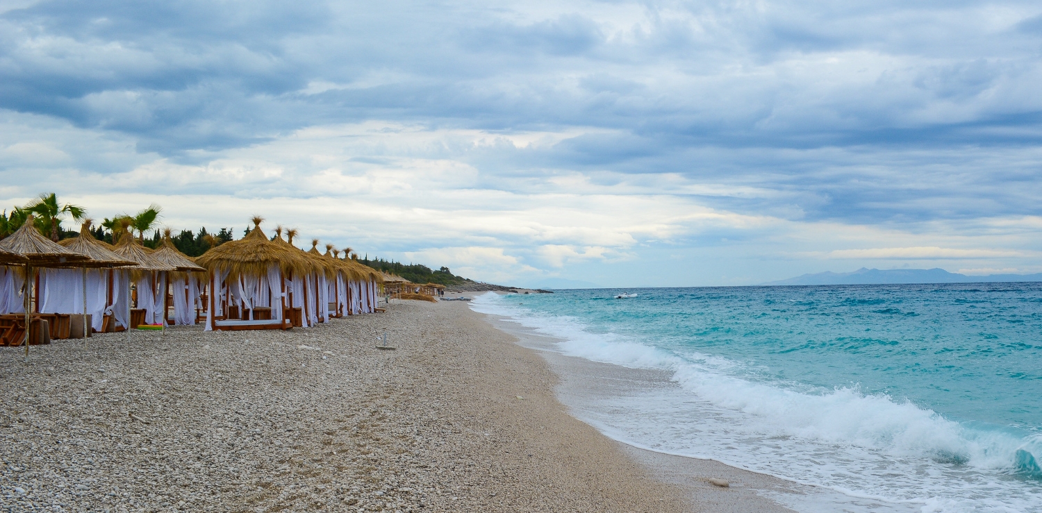 Drymades Beach Albania — beach clubs and boats on the clear Ionian water with limestone mountains above